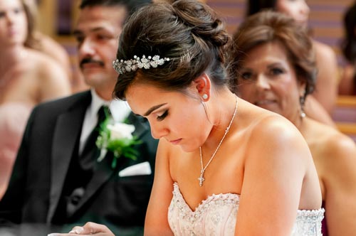 Close-up portrait of a Quinceañera in prayer during a religious ceremony, featuring an ornate tiara and cross necklace, photographed by Eliot Khuner.