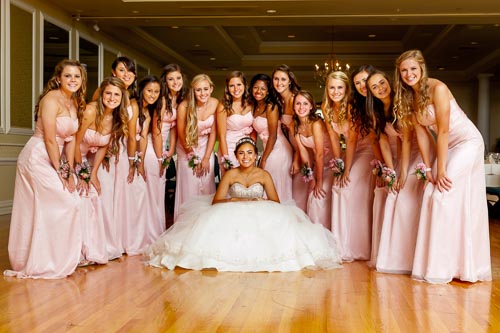 A large Quinceañera court of honor posing in matching pink dresses around the celebrated young woman in a white ballgown on a Diablo Valley dance floor