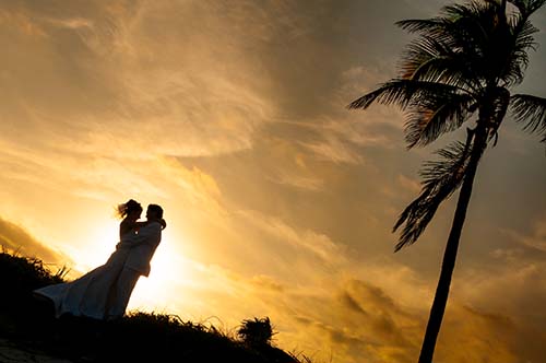Breathtaking silhouette of a wedding couple under a palm tree against a vibrant golden sunset sky.