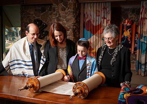 Family standing together at a synagogue during a Bar Mitzvah ceremony with an open Torah scroll, event photography in Berkeley by EK Photo.