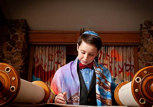 Close-up of a boy in a colorful tallit and kippah reading from the Torah during his Bar Mitzvah celebration in Berkeley, California.
