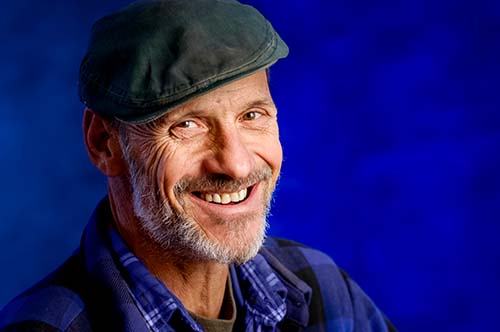 Close-up studio portrait of a smiling man with a gray beard and flat cap, professional photography by EK Photo in Berkeley, CA.